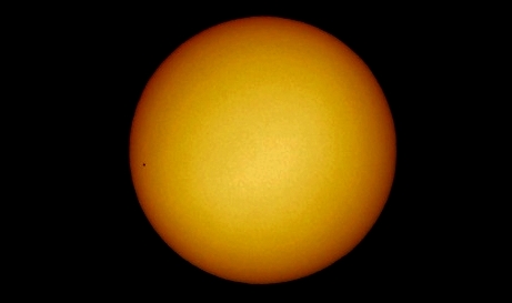 The November 11th, 2019 Mercury transit using a compact digital camera handheld behind the ocular; the transit is seen few after it began (Nikon S3100 compact digital camera handheld at the 20-mm ocular of a Perl 60mm refractor with a solar filter in sheet at the instrument's aperture (yielding a 35x power); picture edited and colorized with a image editor; home observatory)